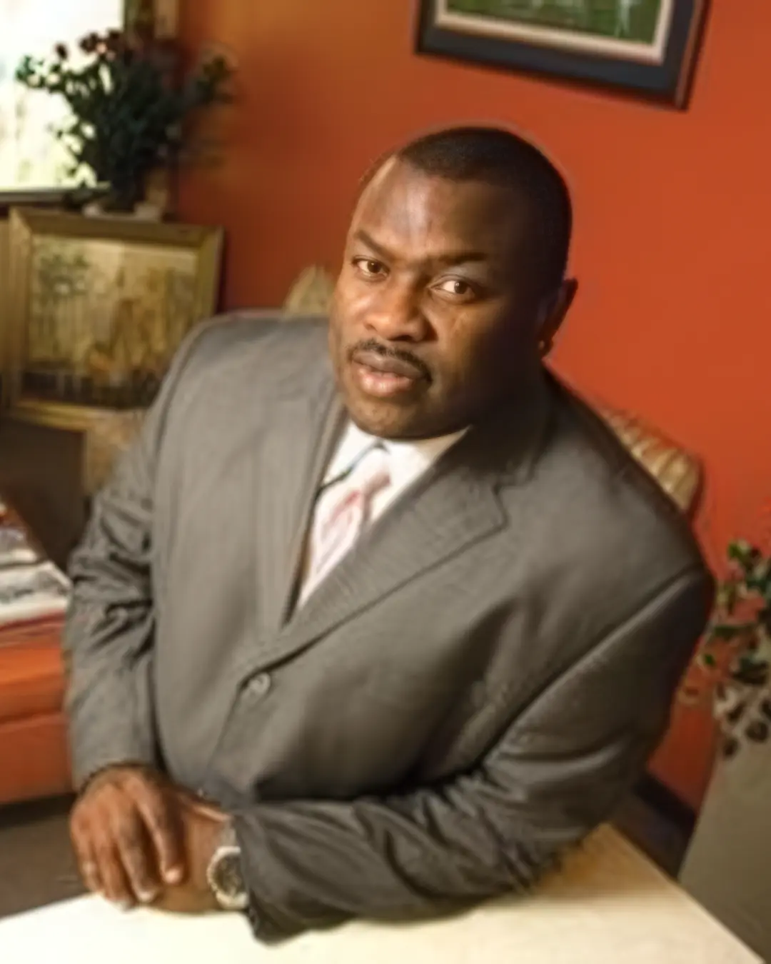 Terrill L. Hill seated at a table in his Palatka office, in a grey suit and tie, looking toward the camera.